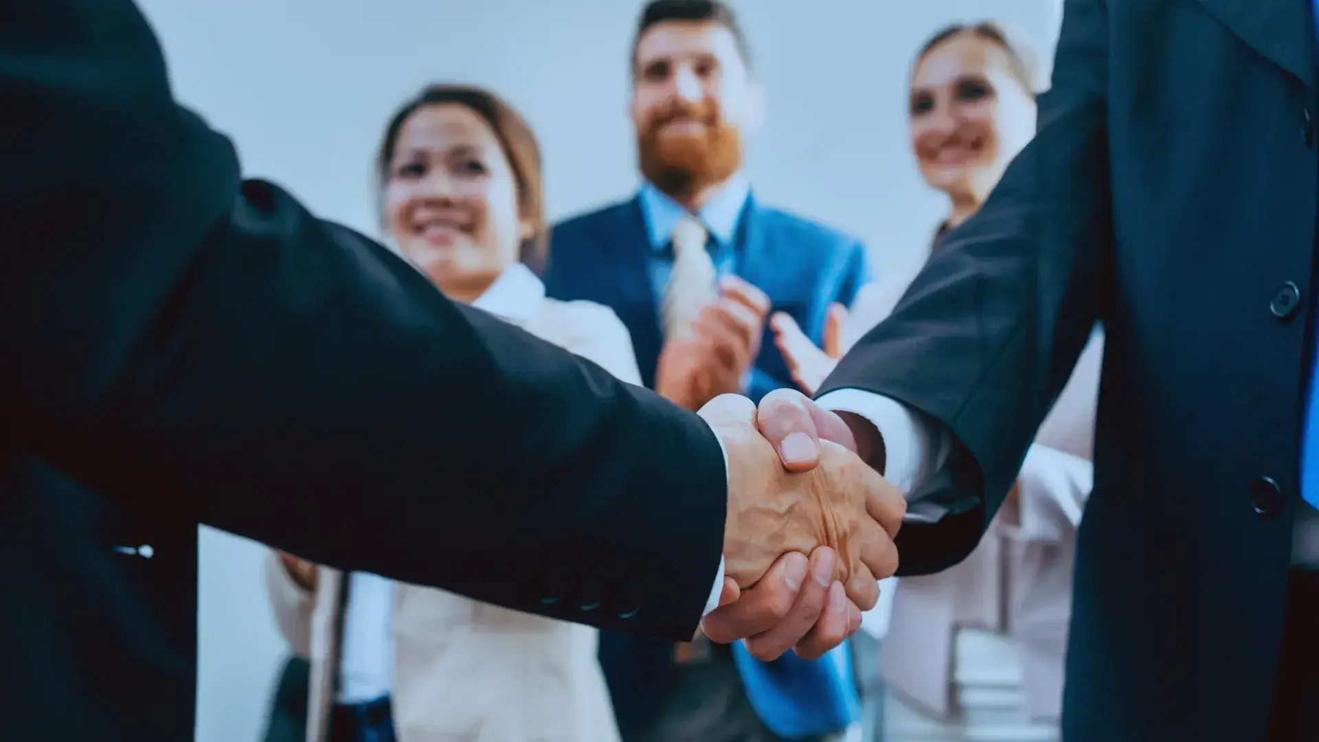Business handshake at a seminar with participants clapping in the background.