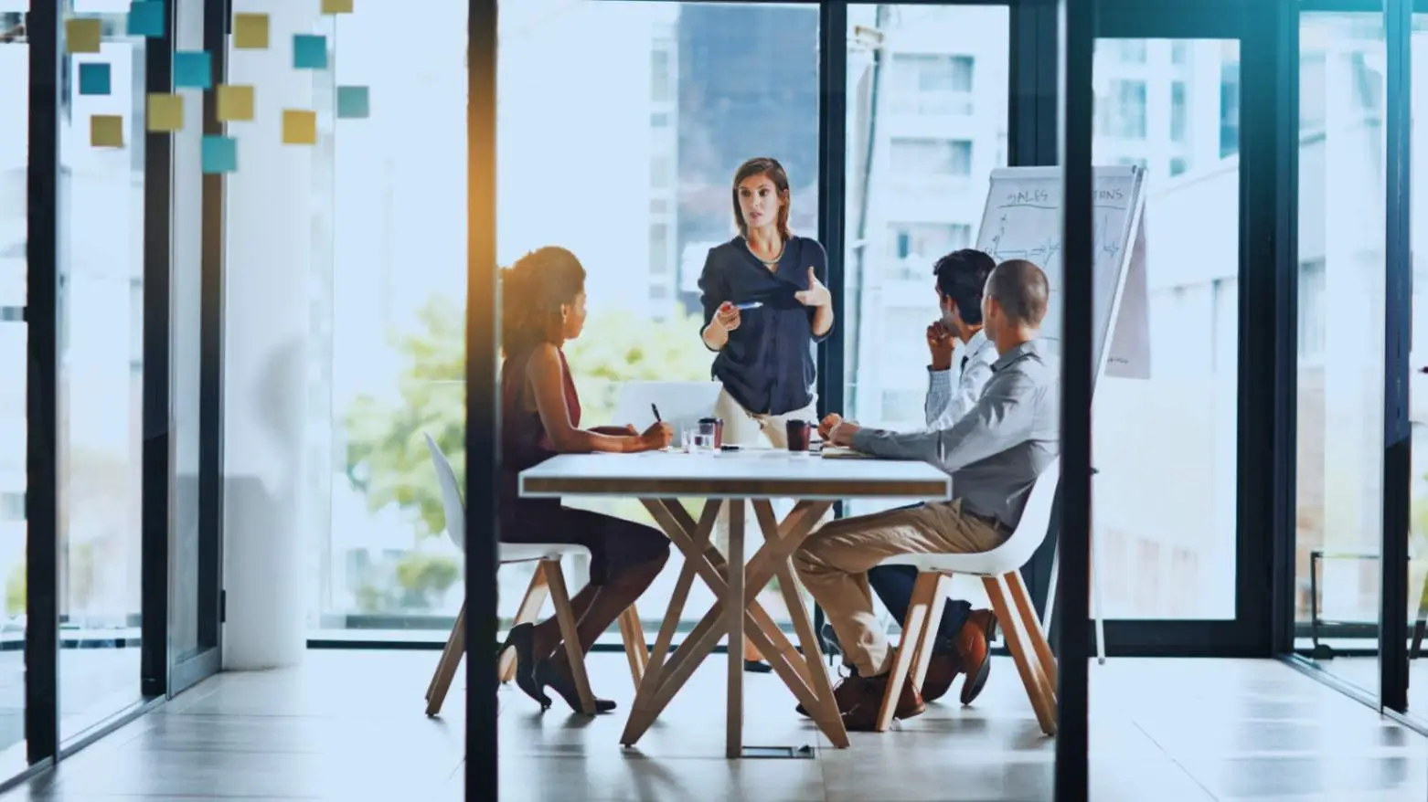 Dynamic business team engaged in a strategic meeting with a female leader gesturing, in a modern, glass-walled office space