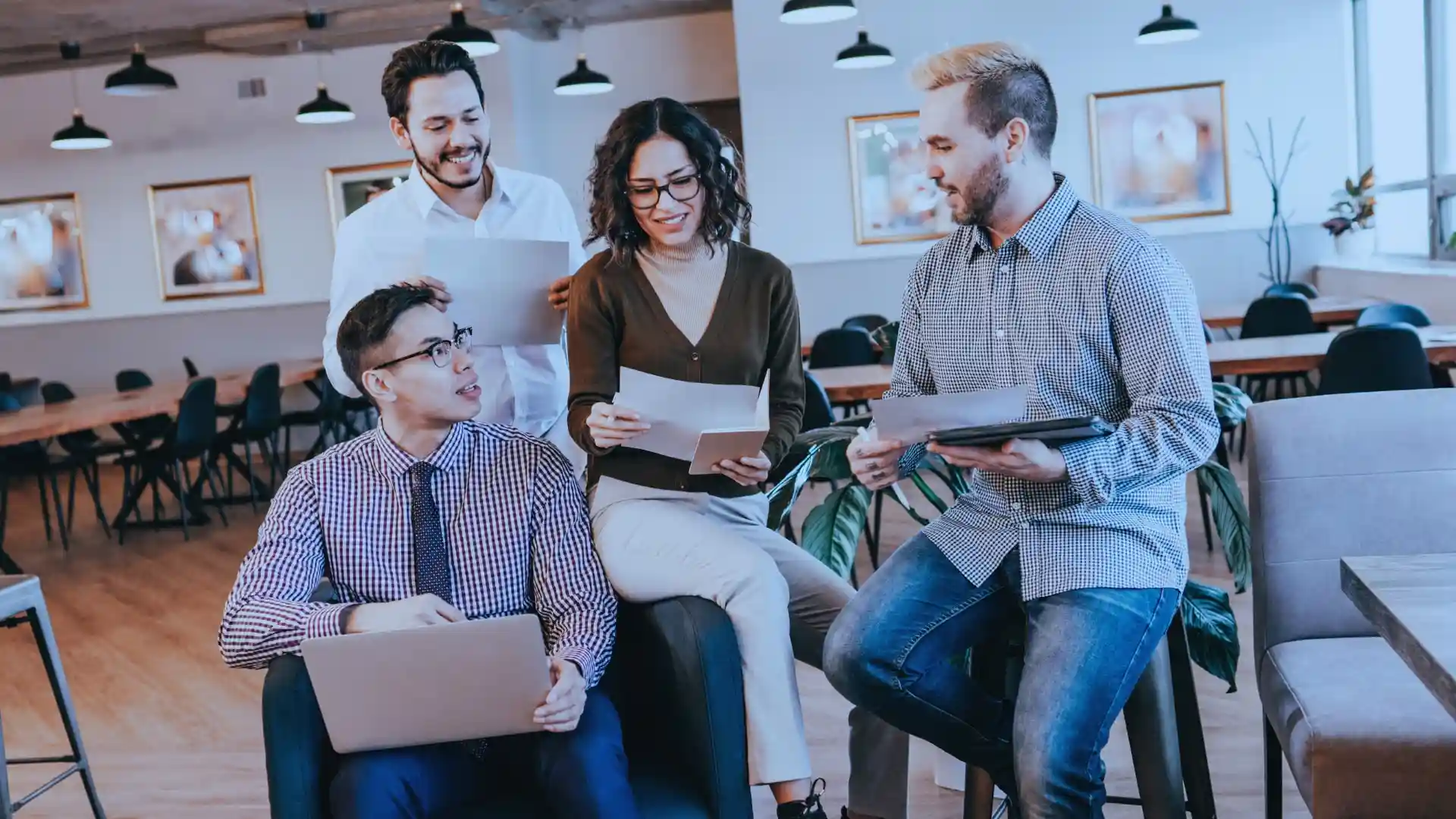 Enthusiastic workgroup with documents discussing project details in a friendly office lounge, fostering team collaboration.