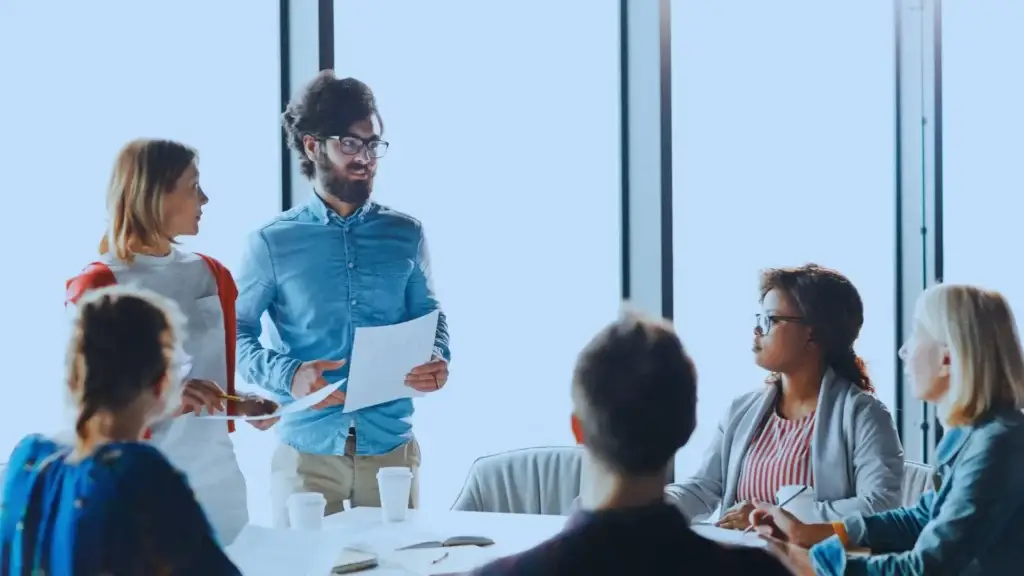 Creative workplace team in a meeting with a man presenting a document, representing active engagement and idea sharing in a corporate environment.