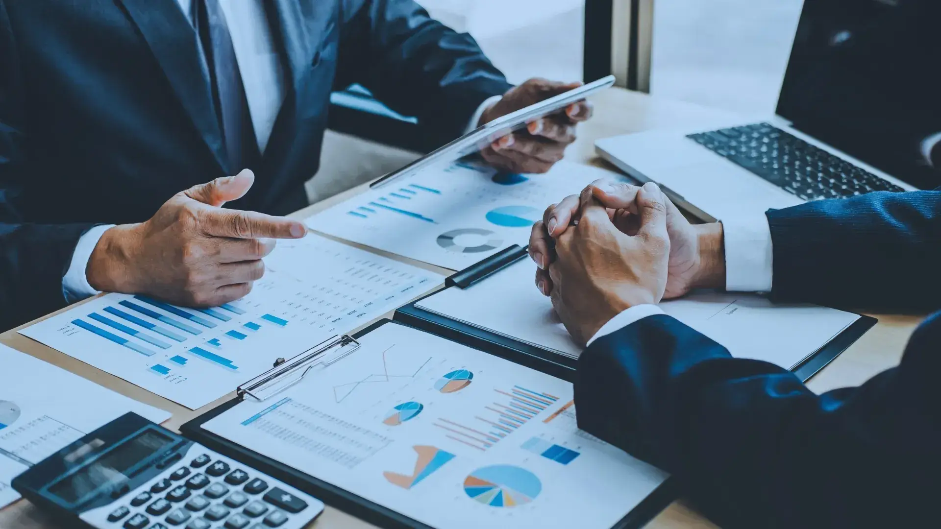 Business professionals discussing over a document, with a focus on hands pointing at a resume, suggesting job interview or agreement review.