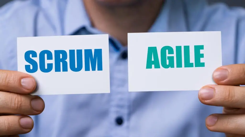 Two hands holding cards with 'SCRUM' and 'AGILE' written on them, depicting a comparison or decision between two project management methodologies.
