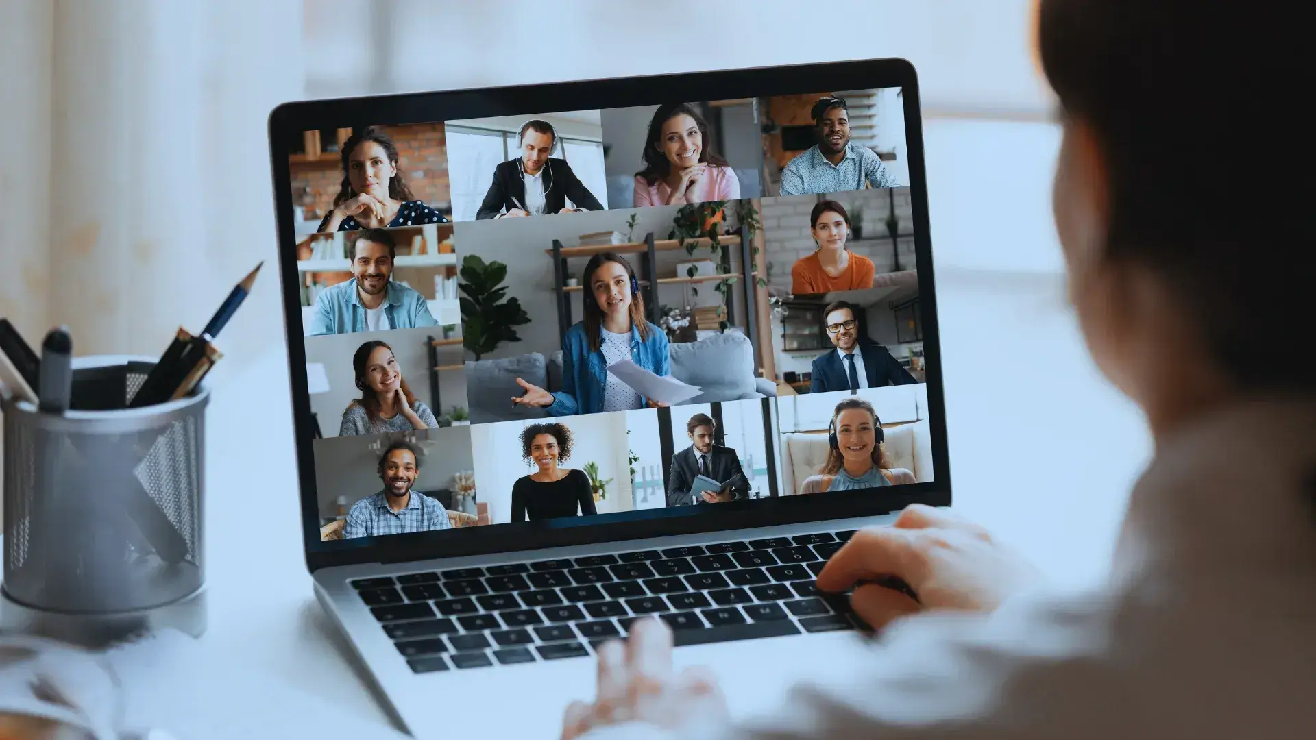 "Rear view of a person attending a virtual team meeting on laptop with diverse participants, indicating global connectivity and the modern approach to remote teamwork."