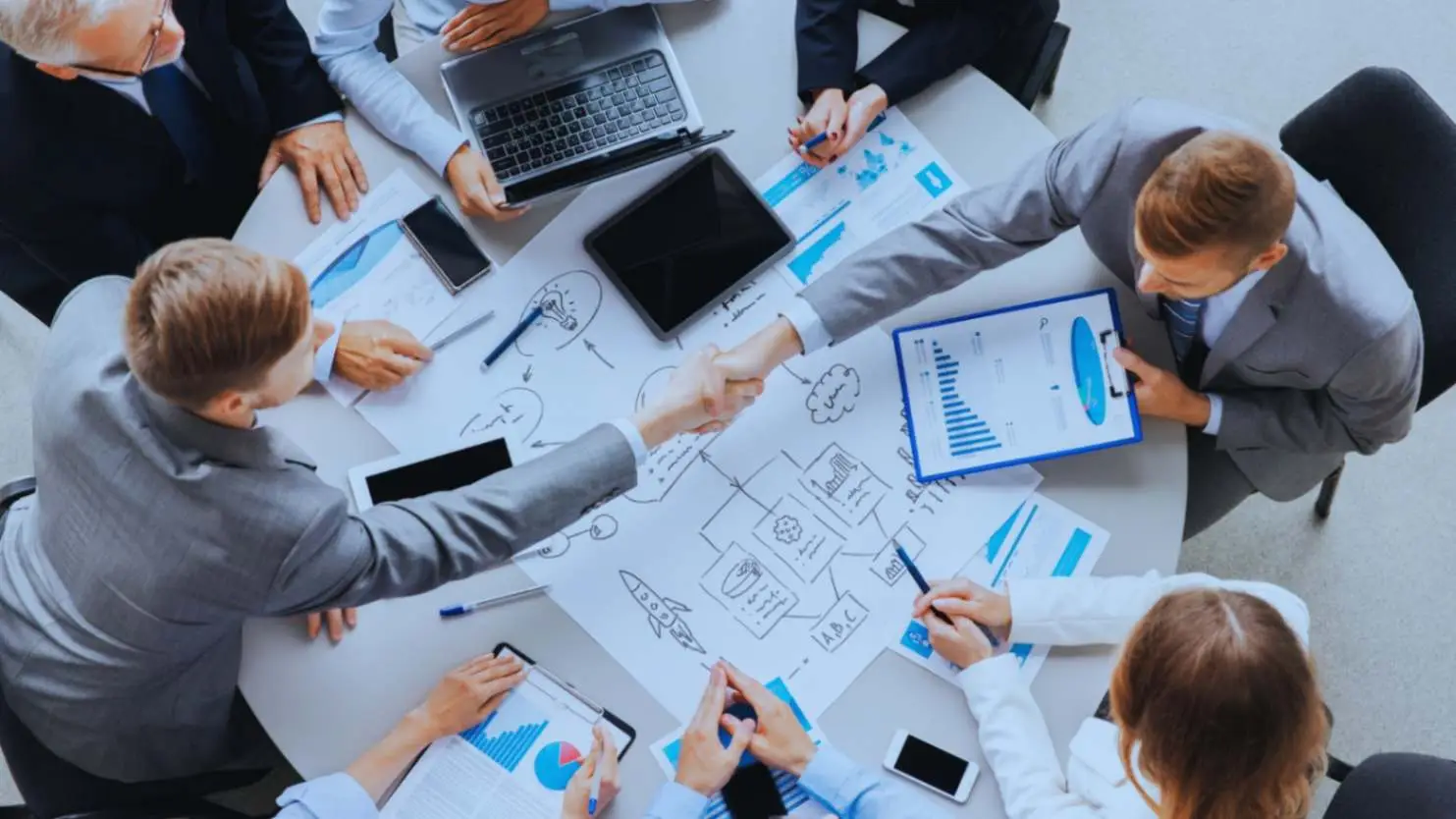 "Top-down view of a business team collaborating around a table filled with charts and gadgets, indicative of Adaptive Project Management strategies."
