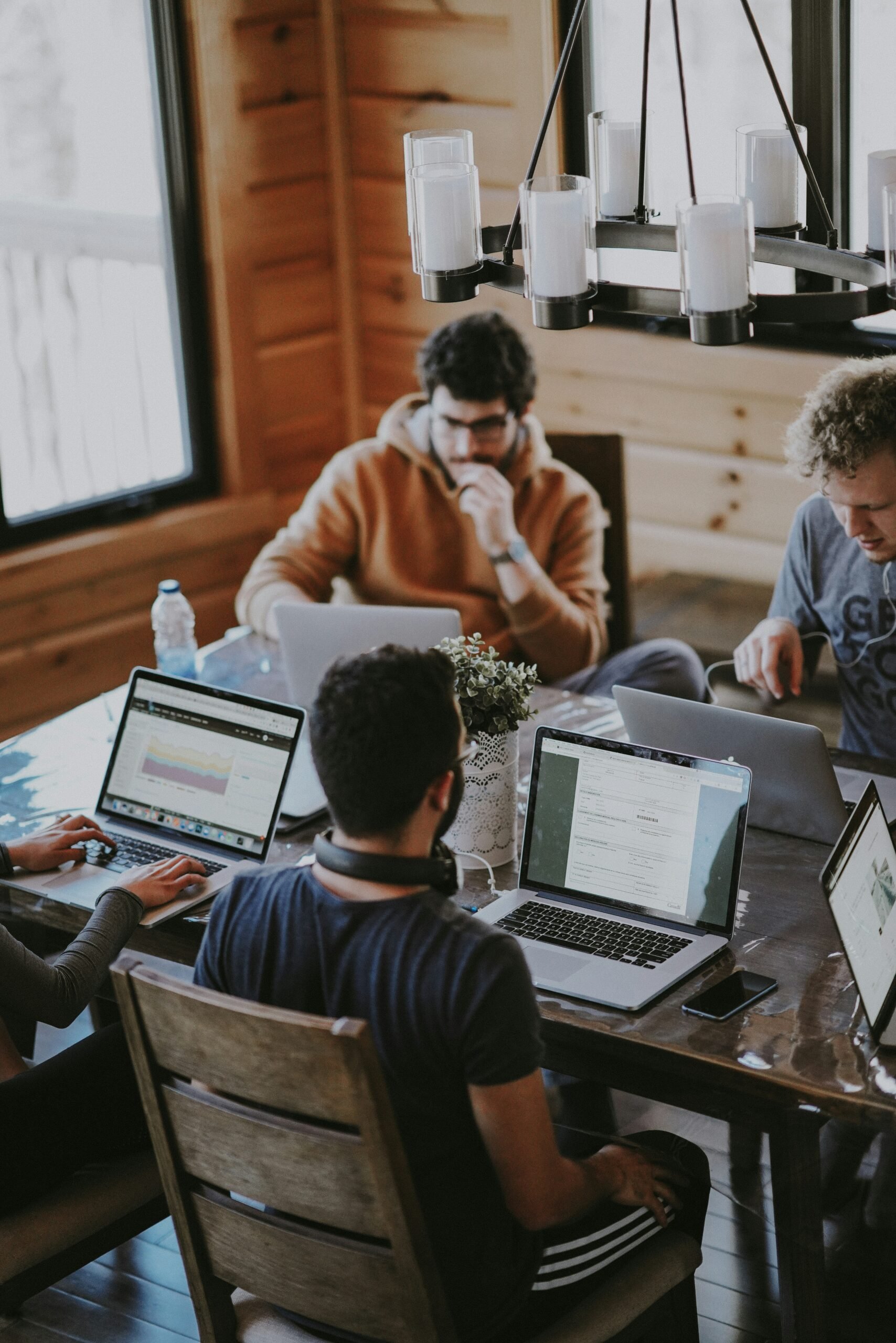 Group of young professionals working on laptops around a table in a cozy wooden workspace.