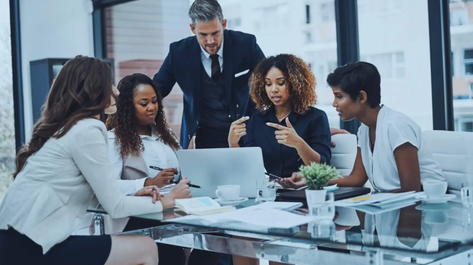 Business meeting showing project communications management with diverse professionals discussing project details around a glass table.