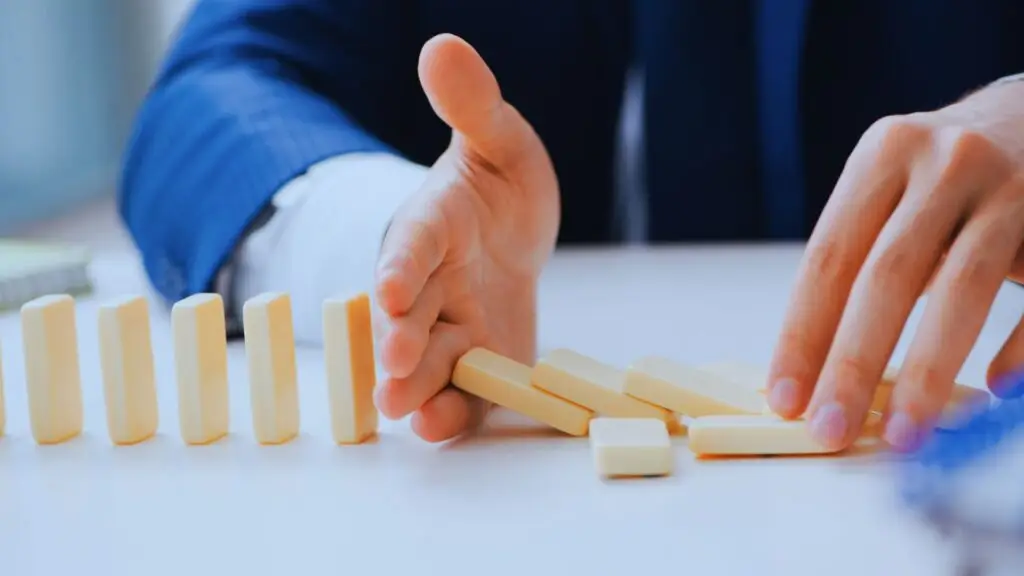 Hand stopping falling dominos in a chain reaction, symbolizing project risks management.