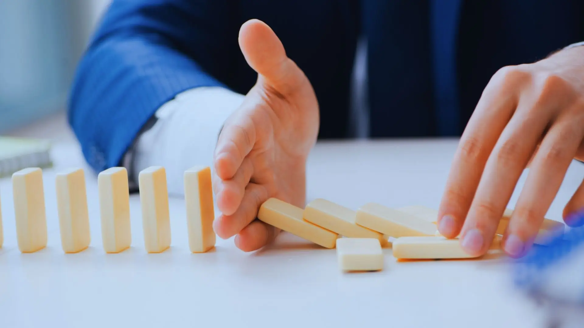 Hand stopping falling dominos in a chain reaction, symbolizing project risks management.
