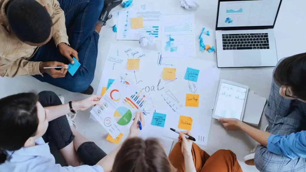 Creative team brainstorming with colorful sticky notes and charts on floor showing teamwork and project planning.