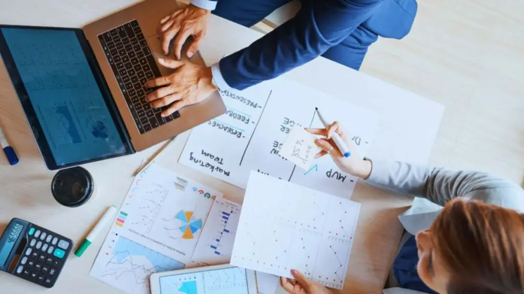 A team of professionals working together on a laptop and reviewing various charts and documents, representing collaborative procurement planning.