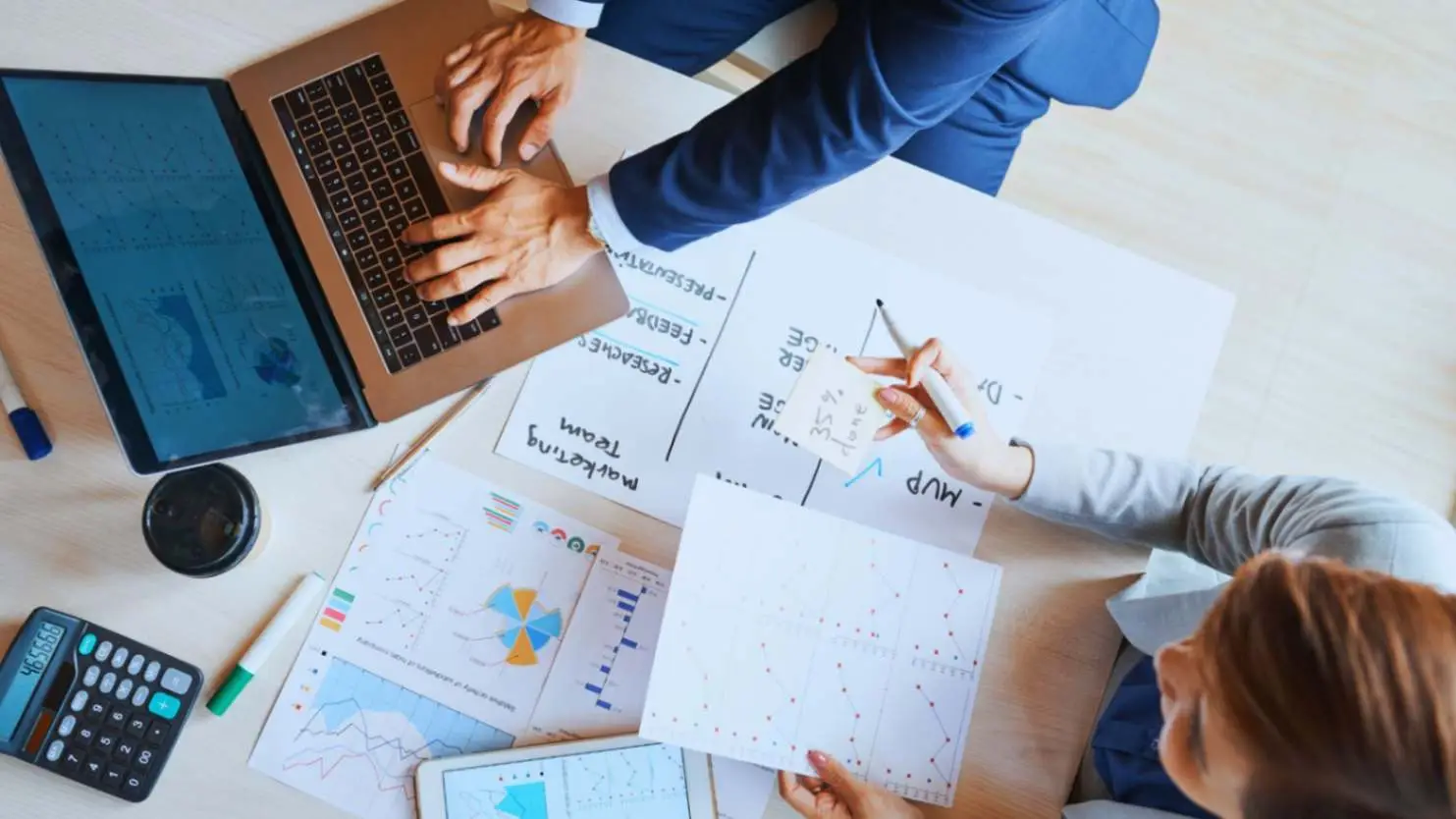 A team of professionals working together on a laptop and reviewing various charts and documents, representing collaborative procurement planning.