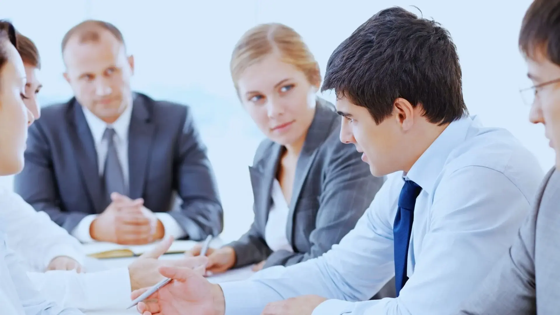 Four business professionals, three men and one woman, sit at a conference table engaged in discussion. They appear focused and attentive during the meeting, possibly reviewing project management solutions like Monday.com Price options.