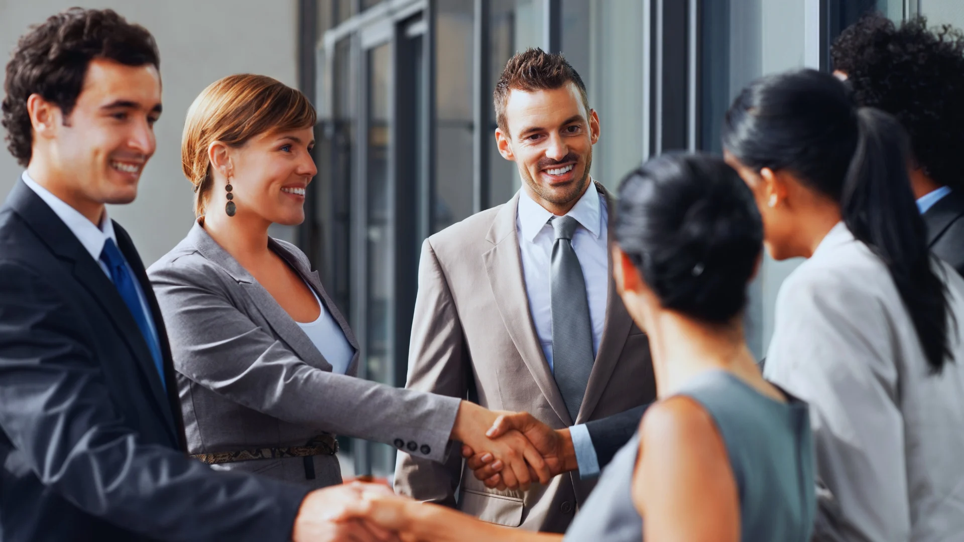 A group of business professionals in formal attire stand indoors, smiling and shaking hands, reflecting a successful agreement built on effective PMI Stakeholder Analysis.