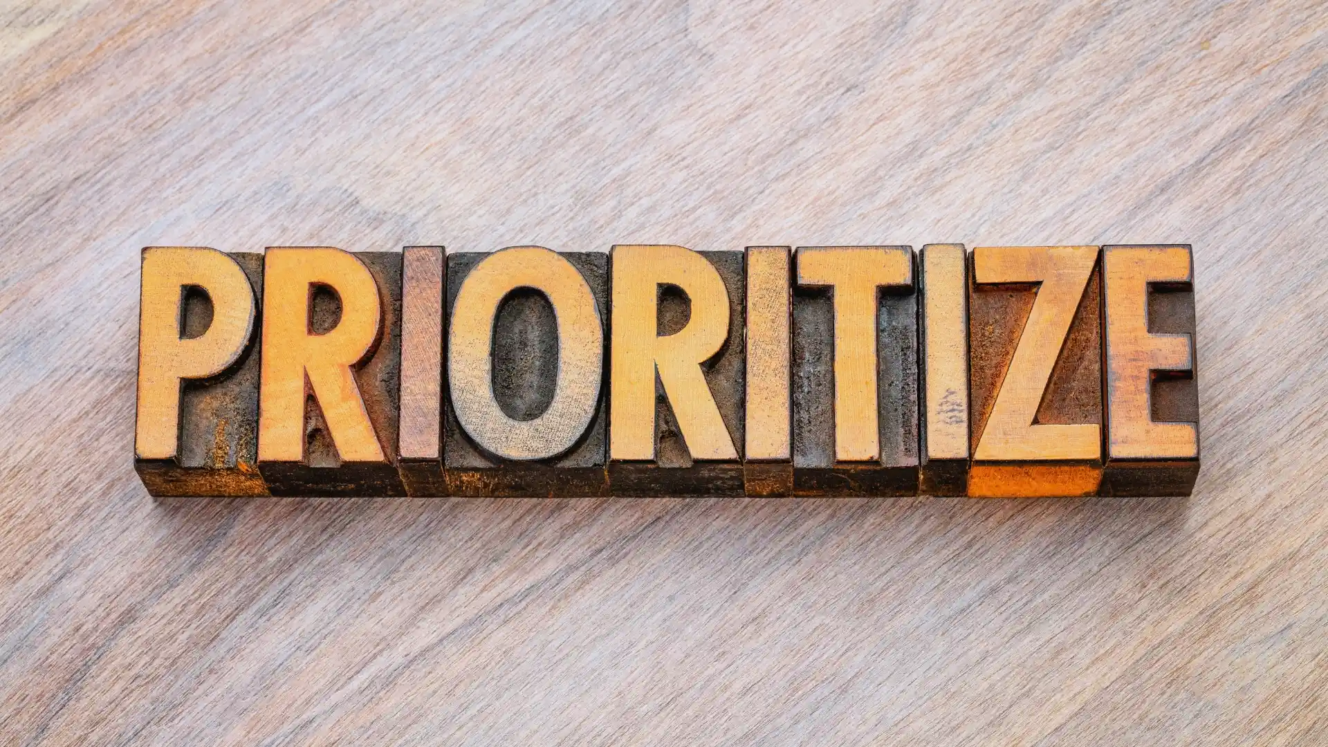 The word "PRIORITIZE" is spelled out in bold, vintage wooden letter blocks on a light wooden surface, emphasizing the importance of Planning in Agile.