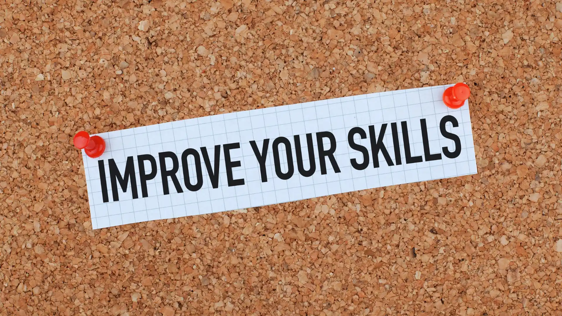 A piece of graph paper with the words "IMPROVE YOUR AGILE SKILLS" is pinned to a corkboard with two red push pins, one on each end of the paper.
