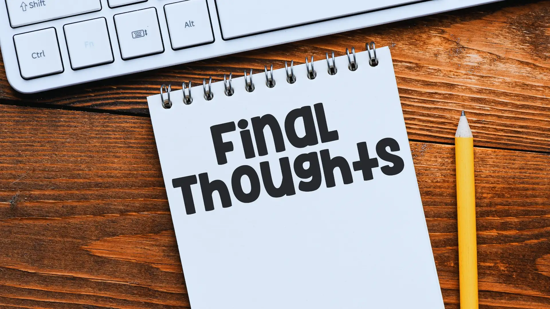 A notepad with the words "Final Thoughts" written in bold letters lies on a wooden desk next to a yellow pencil and part of a white computer keyboard, capturing the essence of reflection and Planning in Agile.