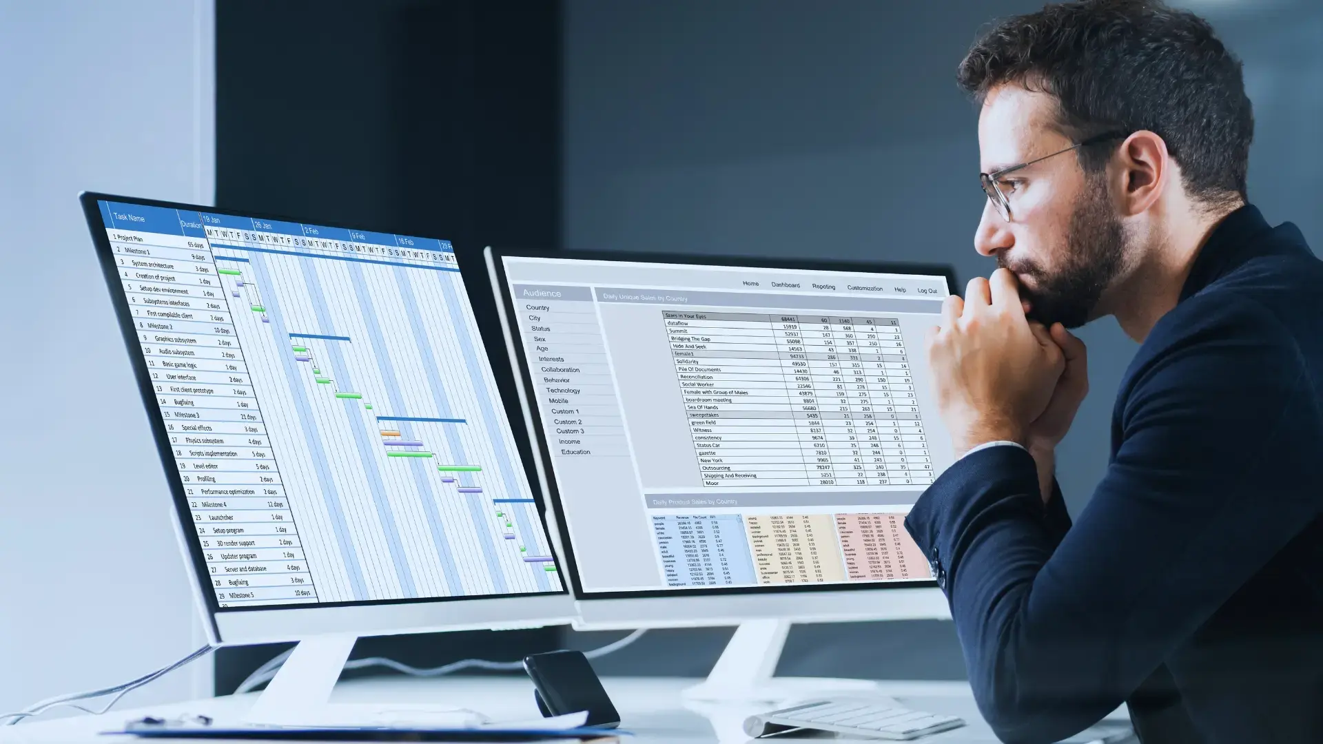 A man in business attire sits at a desk, intently reviewing two large monitors displaying spreadsheets and charts—including a Gantt Chart for Agile Methodology and a data table—in a modern office setting.
