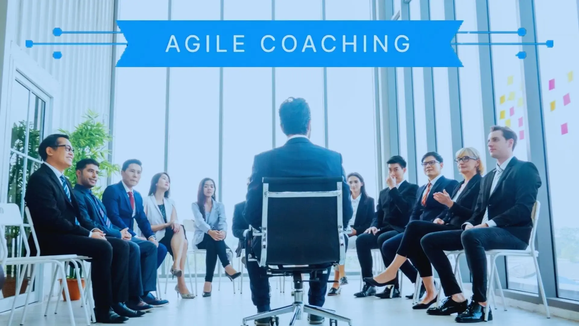 A professional coach sits facing a group of businesspeople in a bright, modern office; the text "Agile Coaching" appears above them on a blue banner, highlighting their collaborative Agile Coaching session.