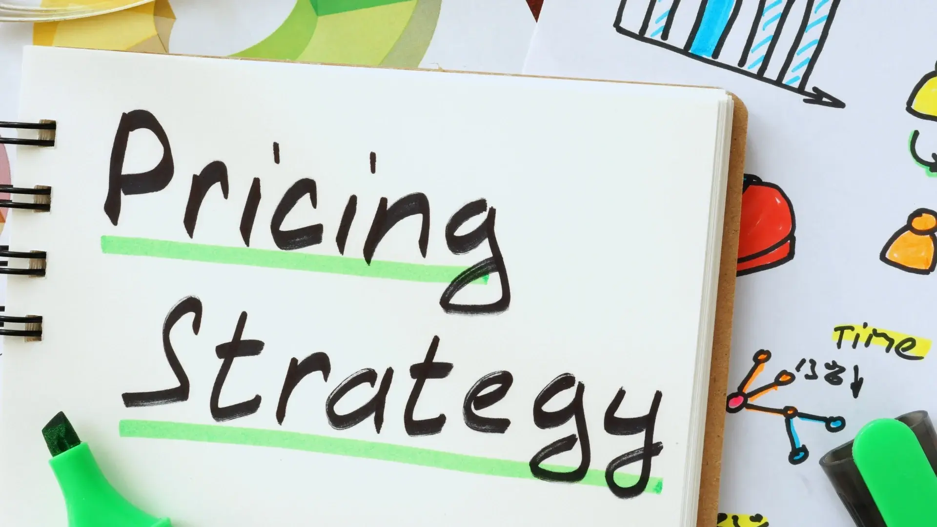 A notebook with the words "Pricing Strategy" written in bold black marker and underlined in green, surrounded by colorful charts, a green marker, and notes comparing SmartSuite vs Todoist.