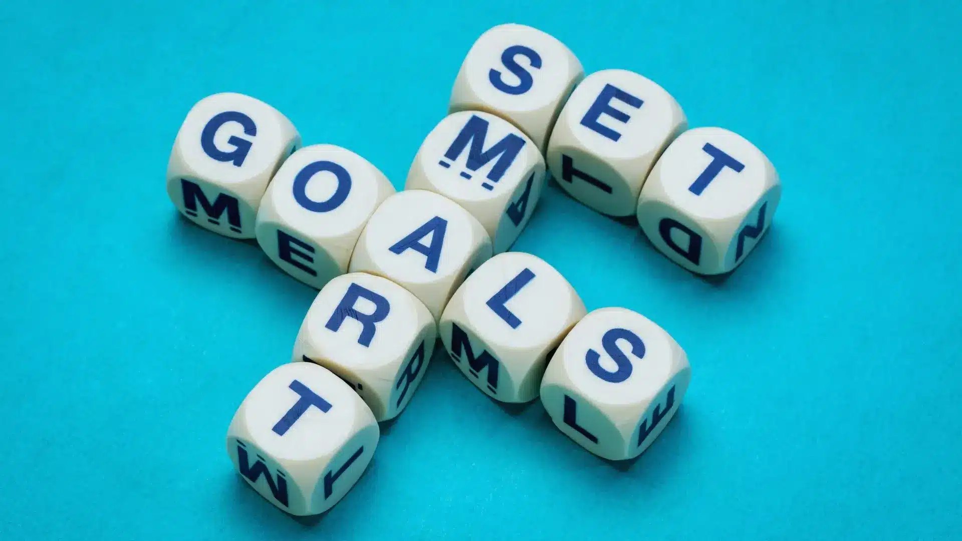Sixteen lettered cubes arranged to spell “SMART GOALS” in a crossword pattern on a blue background, highlighting Goals for Change Management; “SMART” is vertical, intersecting “GOALS” horizontally at the letter “A”.