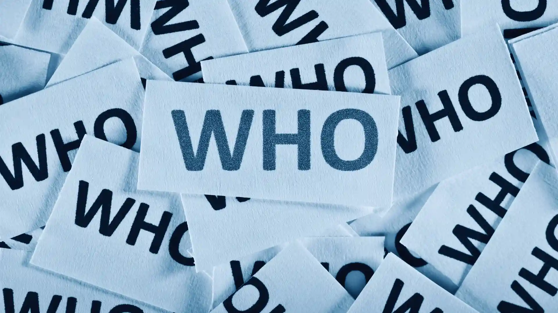 A pile of white paper slips, each printed with the word "WHO" in bold, black letters—one slip featuring "WHO" clearly visible in the center—highlights the clarity that TeamGantt Integrations can bring to your workflow.