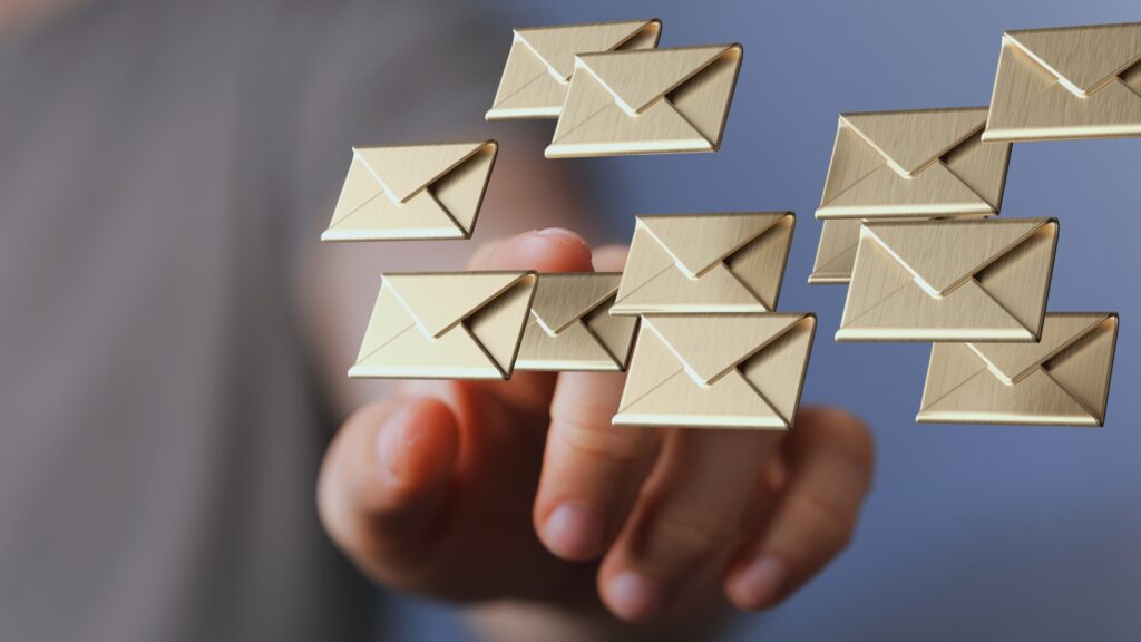A hand reaches toward several floating golden envelope icons, symbolizing email or digital messages—perfect for illustrating a Project Closure Email—against a blurred blue and gray background.