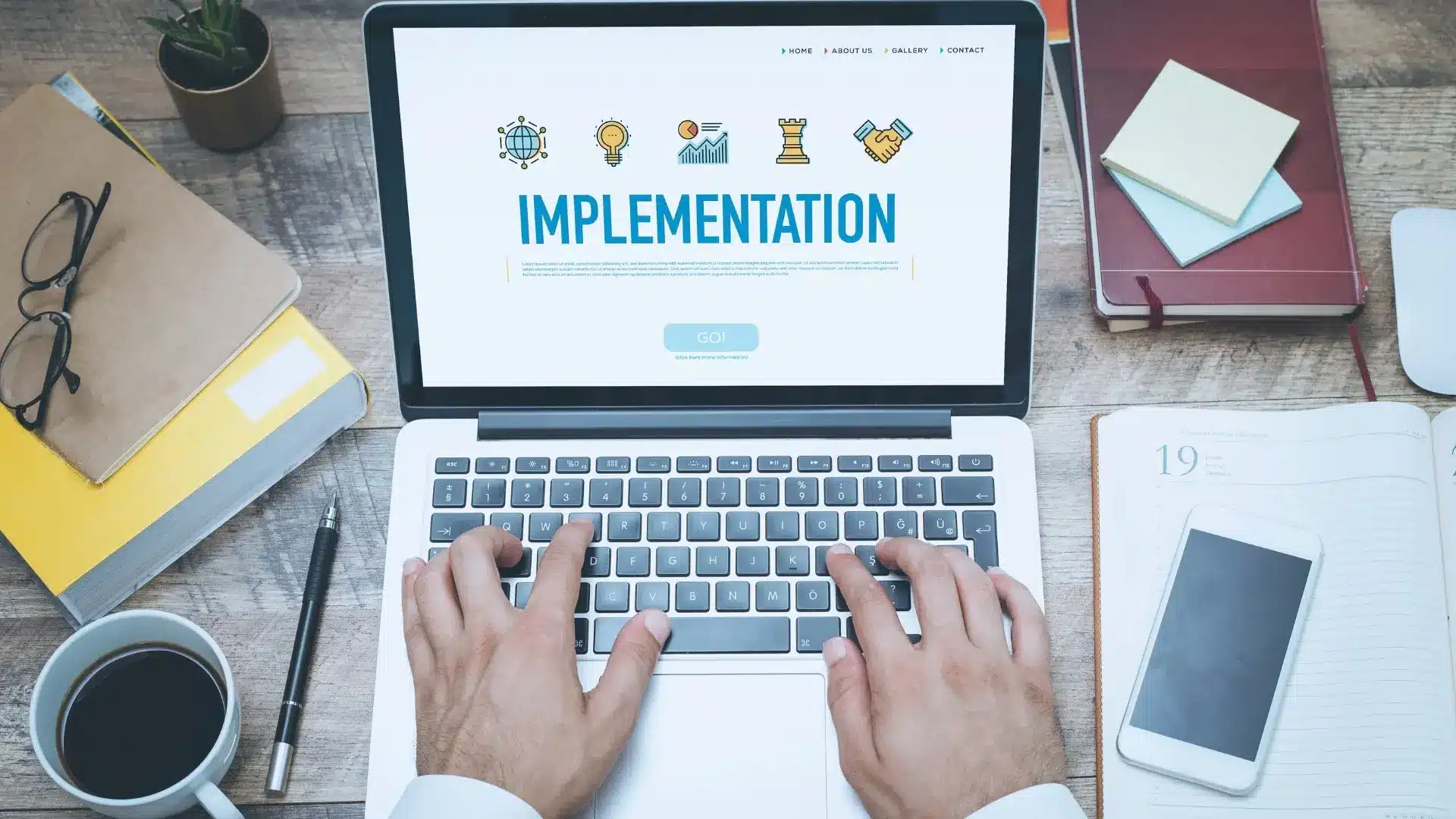 A person types on a laptop displaying "IMPLEMENTATION" with icons above it, surrounded by notebooks, a smartphone, sticky notes, and a coffee cup—illustrating a focus on Value-Driven Delivery at a well-organized wooden desk.