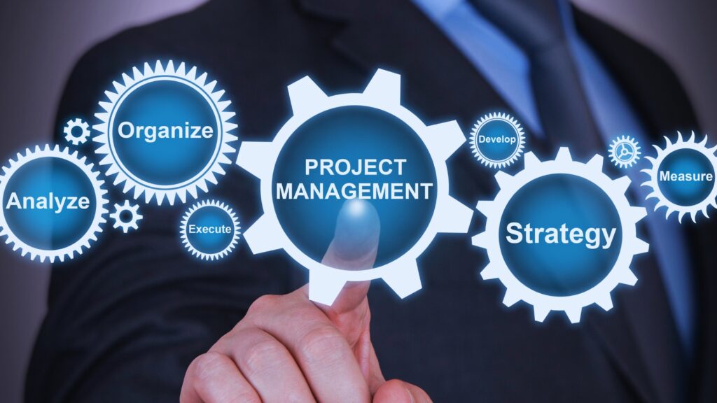 A person in a suit is pointing at a digital interface displaying gears labeled “Project Management,” “Organize,” “Strategy,” “Analyze,” “Execute,” “Develop,” and “Measure”—showcasing a powerful BVDash alternative.