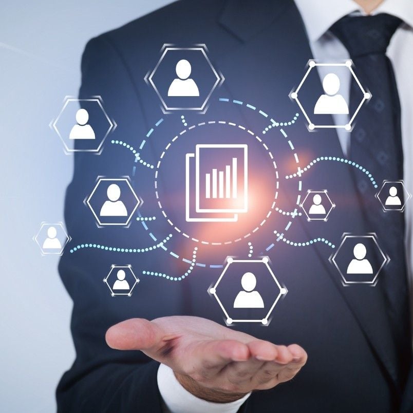 A person in a suit holds out their hand. Above the hand, digital icons show people connected by lines around a chart icon, representing data sharing or networked analytics—much like building a Stakeholder Map for visualizing connections.