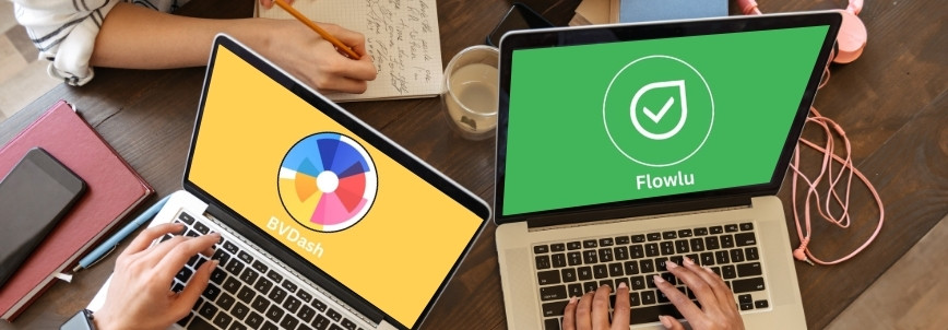 Two people working at a desk, each using a laptop; one screen shows "BVDash" with its colorful logo, while the other displays "Flowlu" with a green background—perfect for those comparing BVDash vs. Flowlu. Notebooks and coffee are on the desk.