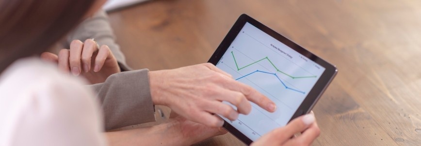 Two people review a tablet displaying a multi-colored line graph, collaborating on data analysis and Project Progress Tracking in BVDash at a wooden table.