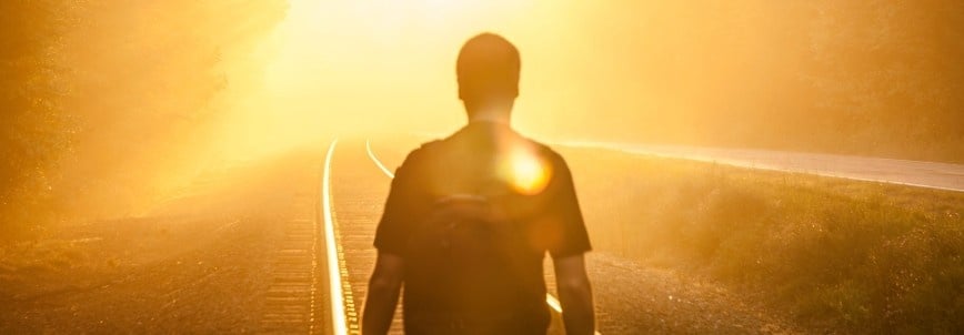 A person with a backpack walks along railroad tracks toward a bright, golden light, surrounded by mist and trees—a scene that feels straight from How to Write an Epic, with its warm, glowing atmosphere full of adventure.