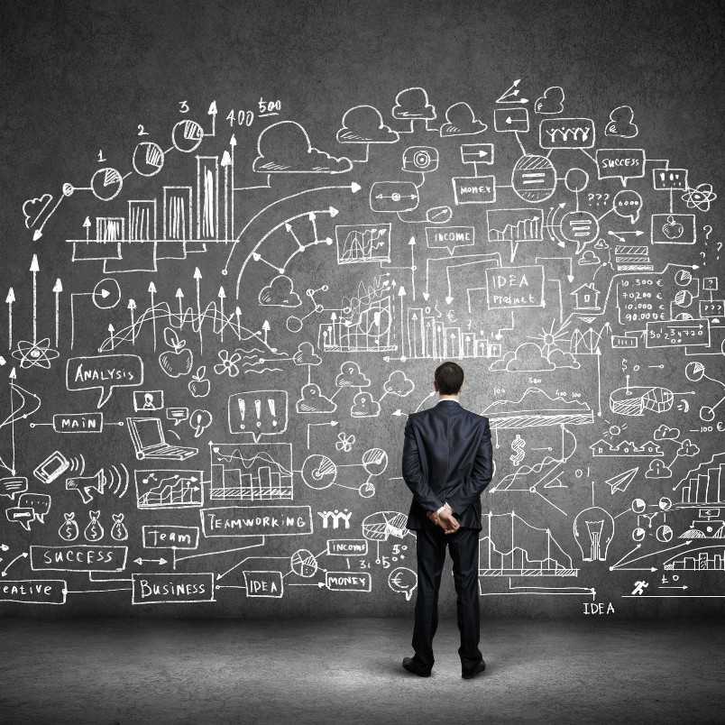 A man in a suit stands before a chalkboard filled with complex business doodles, charts, and diagrams, appearing to analyze or contemplate the data—perhaps creating a stakeholder map to better understand key relationships.