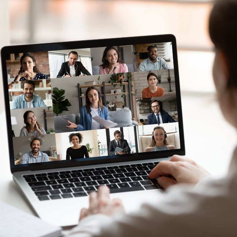A person participates in a virtual meeting on a laptop, displaying twelve diverse people smiling and talking in a grid of video call windows—an ideal scene for project management for remote teams.