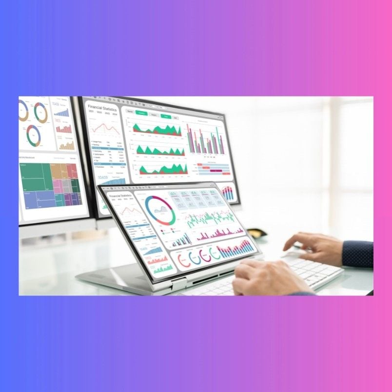 A person working at a desk with a keyboard, using Project Management Software for Small Businesses, views colorful financial graphs and charts on two computer screens. The softly blurred background keeps the focus on analytics.
