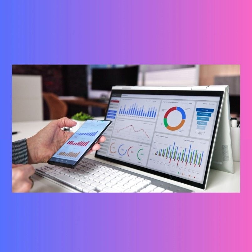 A person holds a smartphone and stylus in front of a tablet displaying colorful charts and graphs, illustrating Project Management Software for Small Businesses, with a white keyboard nearby, all set against a blue and pink gradient background.