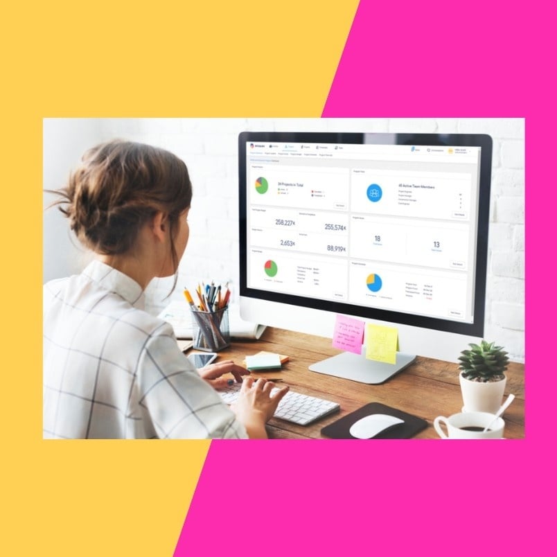 A woman sits at a desk using a desktop computer displaying various charts and Task Management in BVDash analytics. The workspace features office supplies, a plant, and is framed with yellow and pink geometric shapes.