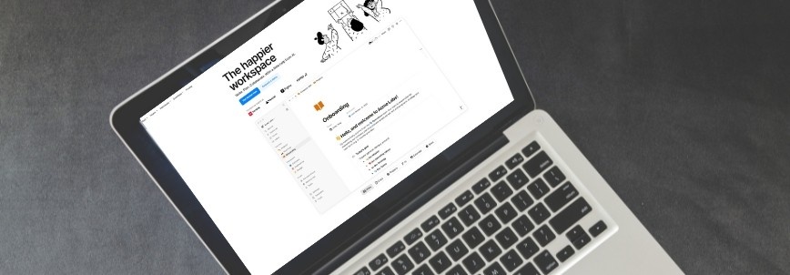 A laptop displaying a Notion workspace titled "The Happier Workspace," with organized notes and folders—including some created using Markdown in Notion—viewed from above on a gray surface.
