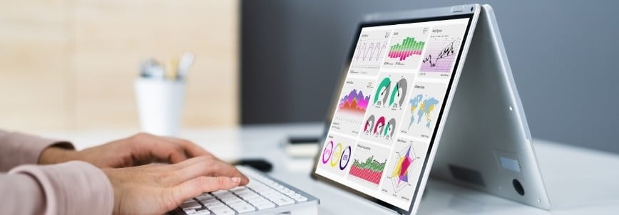 A person using a wireless keyboard sits in front of a tablet in tent mode, which displays colorful charts, graphs, and data visualizations from Reporting Dashboards in BVDash.