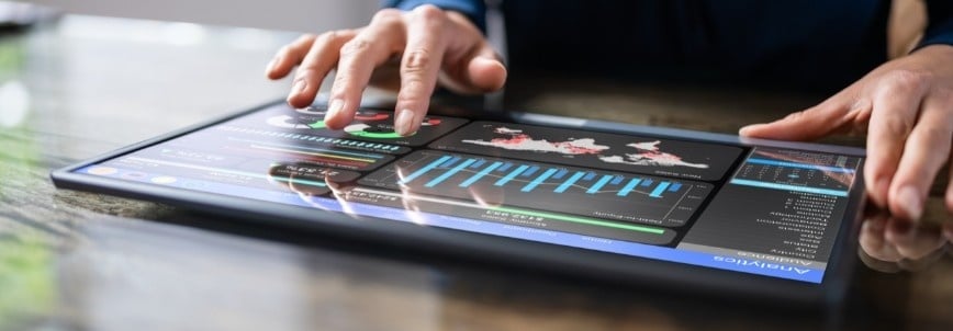 A person uses a tablet displaying interactive data visualizations, including graphs, charts, maps, and Timeline Views in Notion. The screen shows analytics and statistical information on a reflective surface.