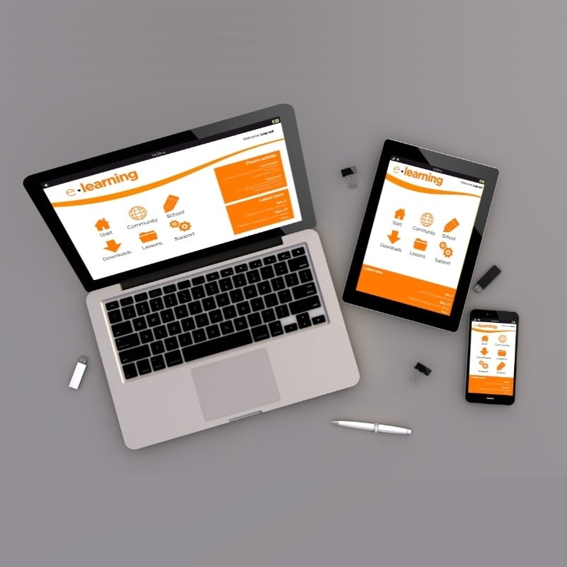 Laptop, tablet, and smartphone displaying a CAPM Exam Preparation e-learning website on a gray surface, with stylus pens and USB drives nearby. The site features orange and white colors with icons for different learning categories.