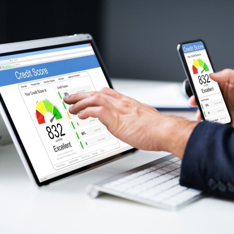 A person checks their credit score on both a laptop and smartphone after completing rosemet capm training, with both screens showing an "Excellent" 832 score and vibrant color-coded gauge graphics.