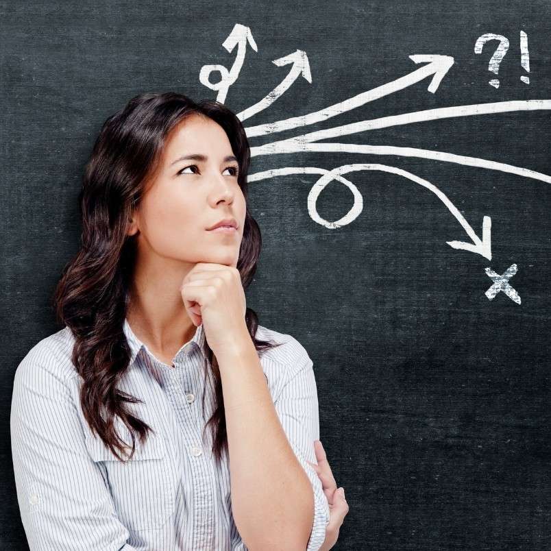 A woman stands thoughtfully in front of a chalkboard with arrows, a question mark, and an X drawn above her head, symbolizing the search for effective decision making tools amid confusion.