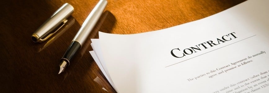 A close-up of a contract management document on a wooden desk next to an uncapped fountain pen, with light shining on the surface.