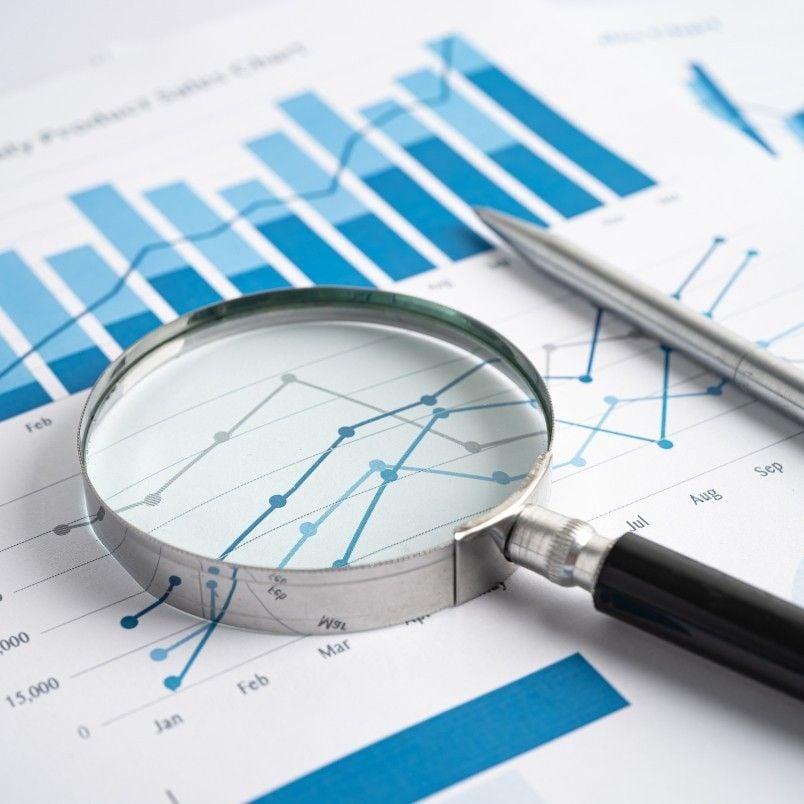A magnifying glass and a pen rest on printed charts with blue bar graphs and line graphs, emphasizing financial data analysis, business statistics, and insights valuable for creating a project charter in an agile environment.