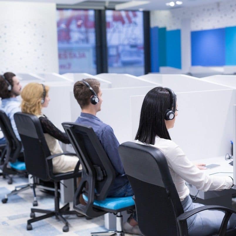 Several people wearing headsets are seated at desks in a modern office space with partitioned workstations, creating an environment similar to the collaborative atmosphere of a PMP Exam Experience.