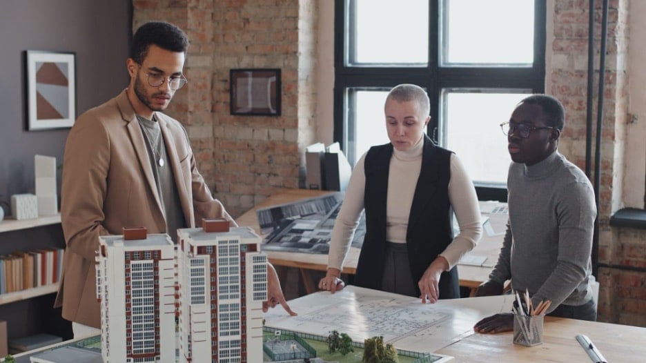 Three colleagues reviewing architectural plans and building models during a project meeting